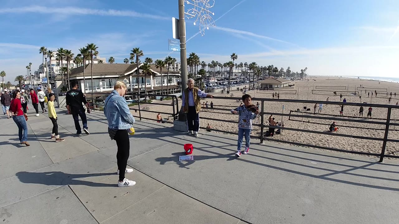 Beachside walkway with a child near a railing and a red bucket on the ground.