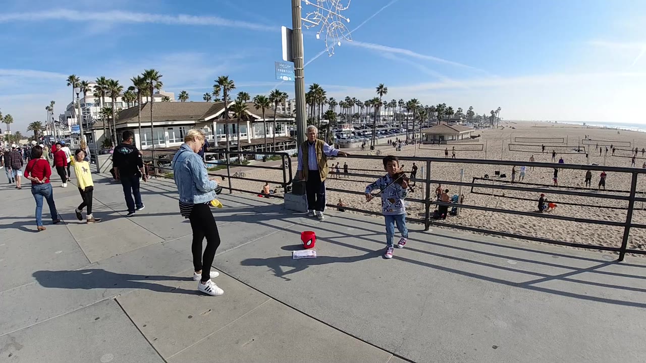 Wide pier scene with child violinist, pedestrians, and sandy beach.