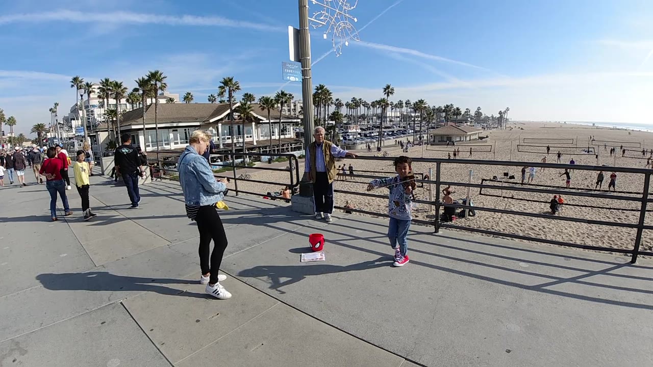 Child performer and onlookers on a bright beach promenade.