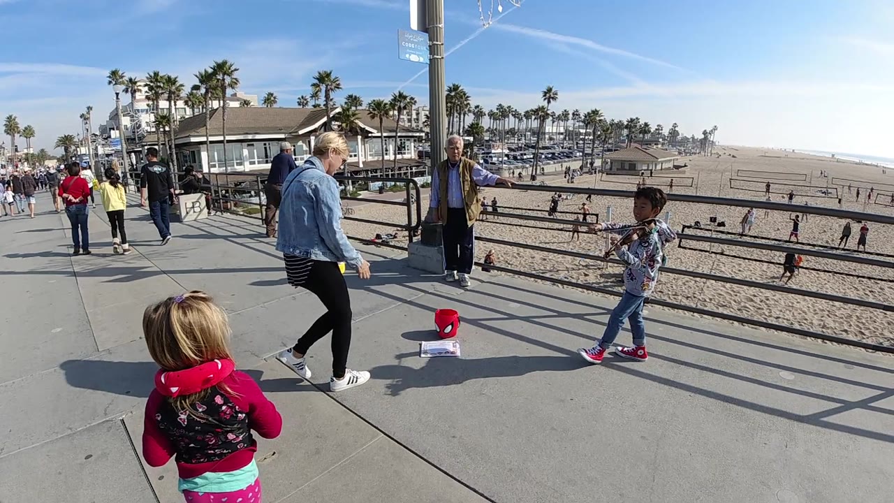 Woman and child on sunny beach walkway with crowd and palms