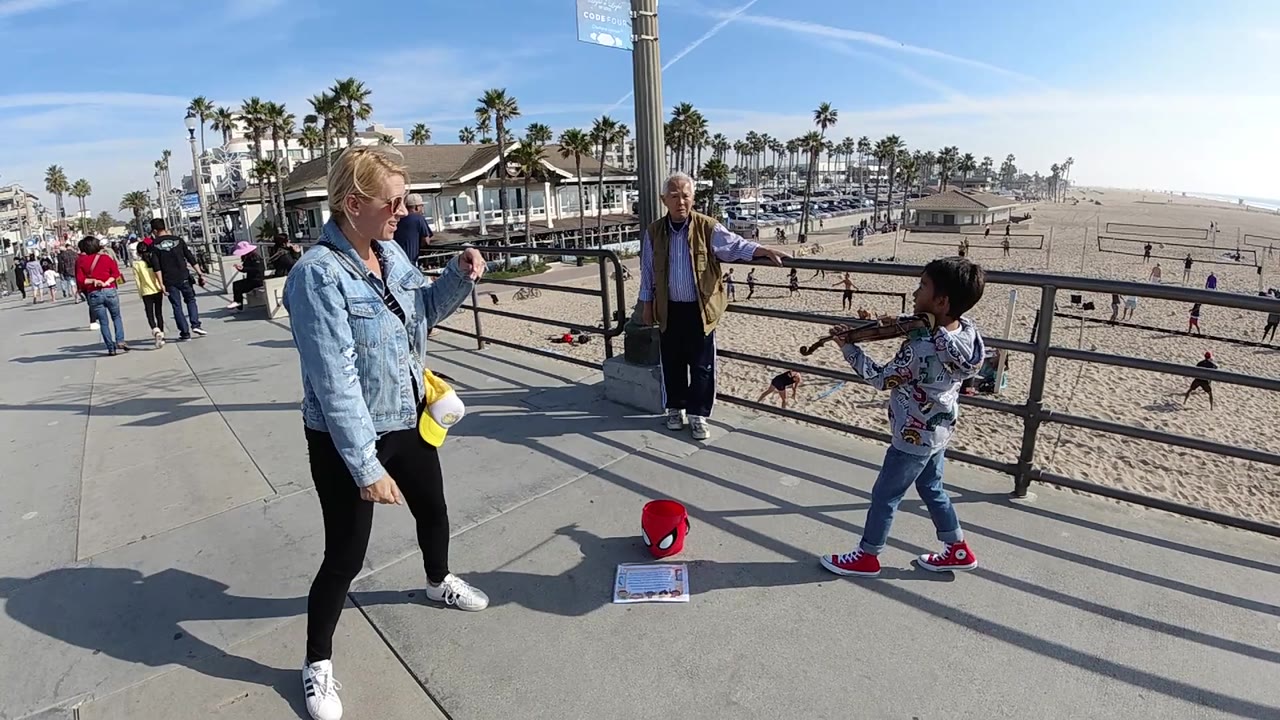 Woman watches a child violinist on a beach walkway.