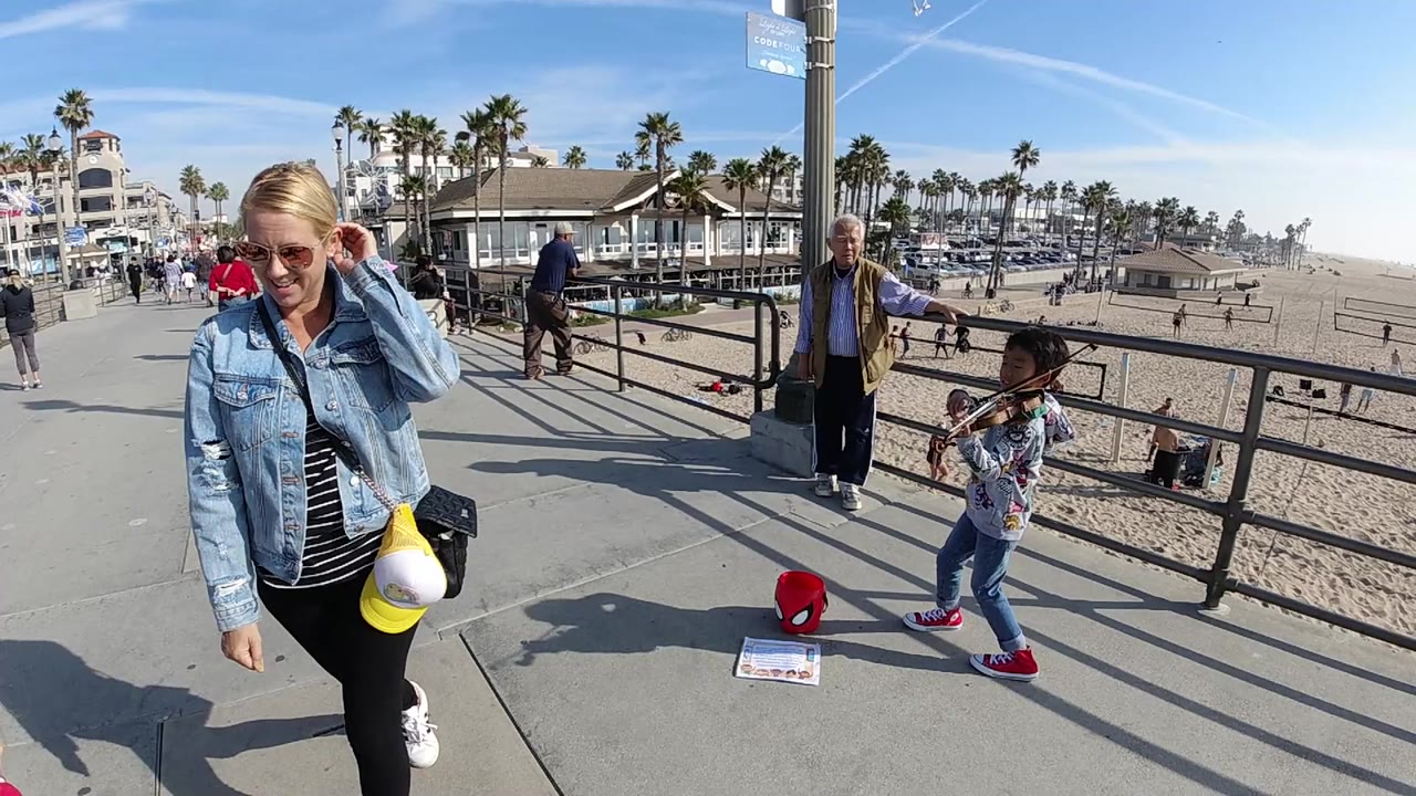 Woman in denim jacket closer to camera beside beach railing and child.
