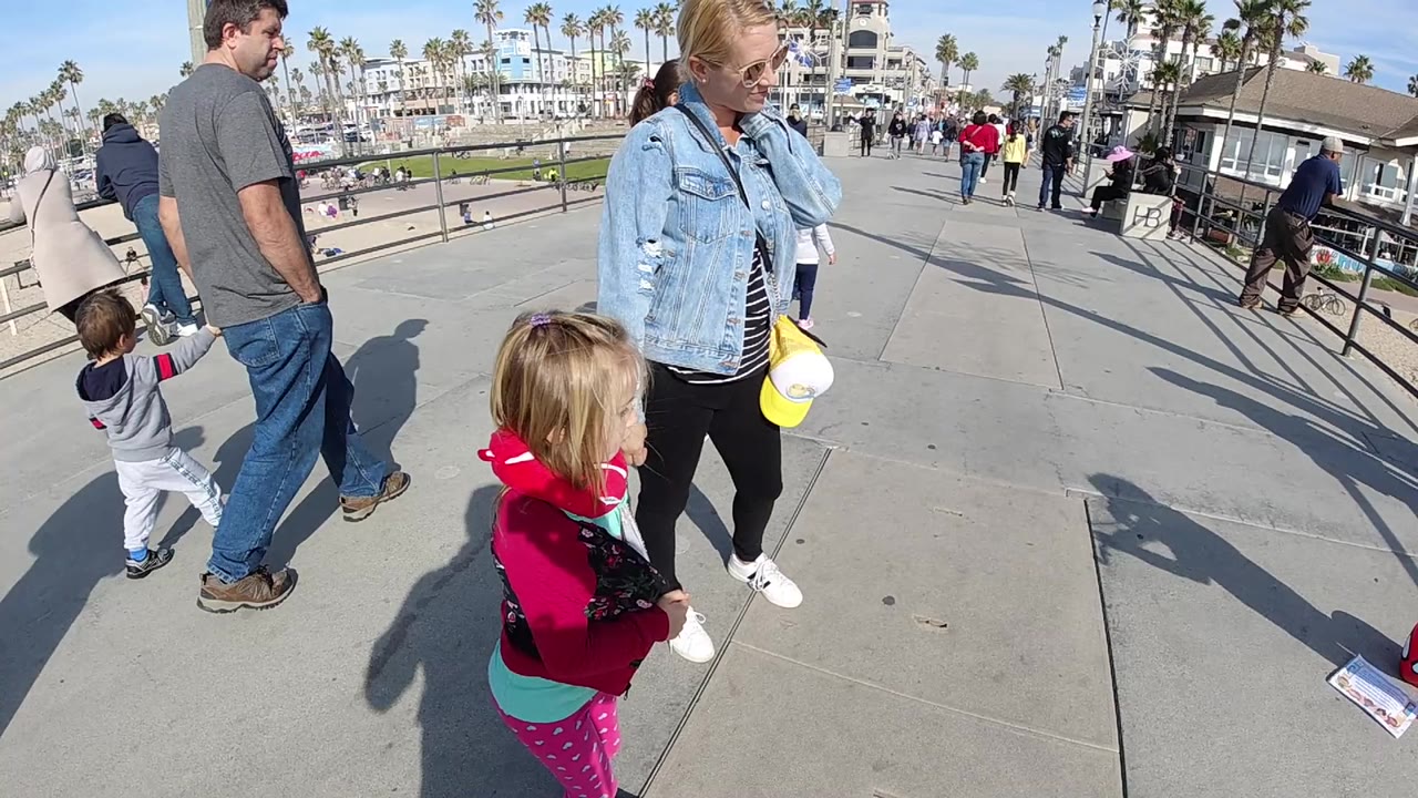 Family group and pedestrians on a paved coastal promenade under bright sun.