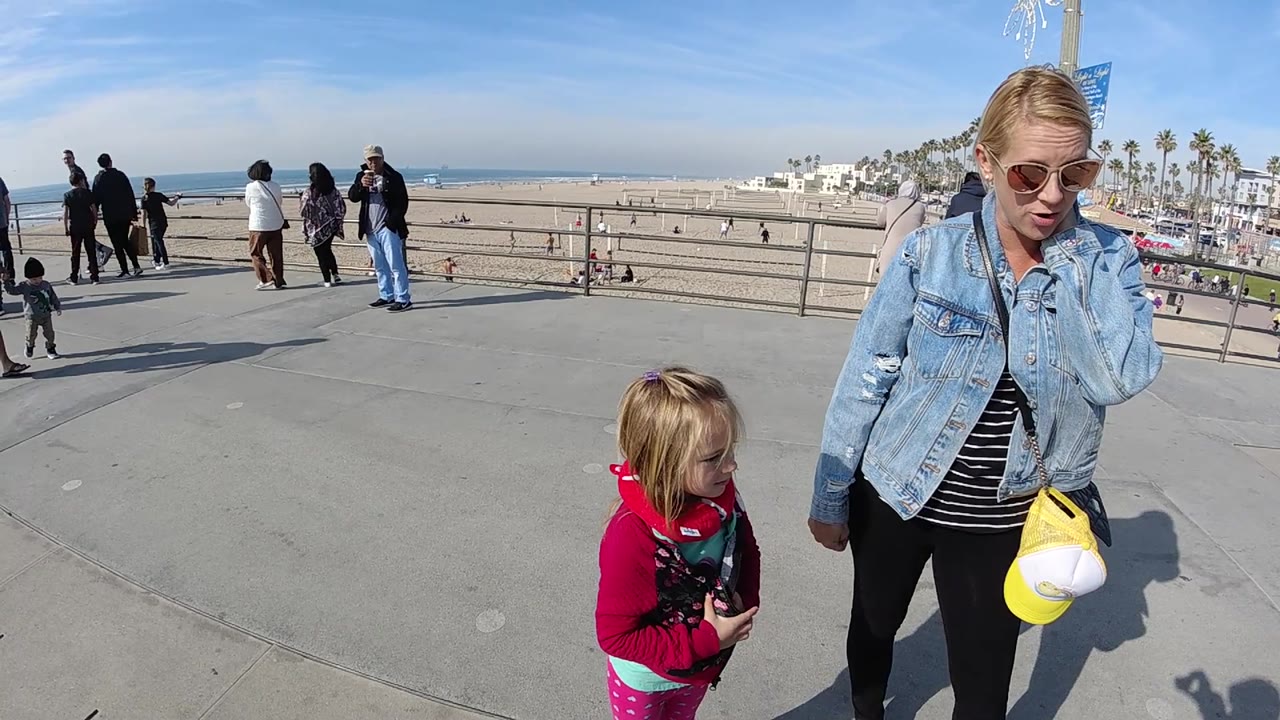 Woman and girl walking on concrete boardwalk beside beach and ocean.