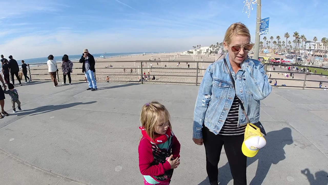 Woman and child on promenade with beach and palm trees beyond.