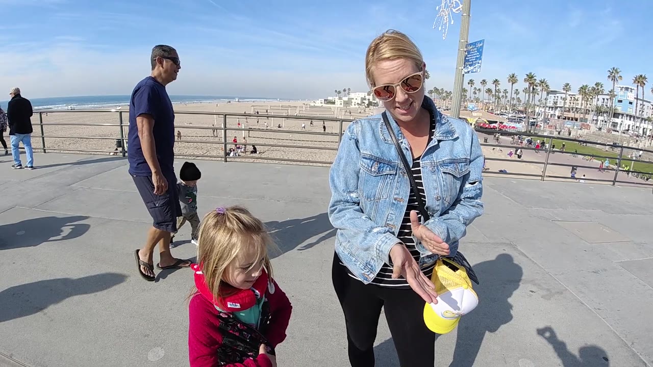Woman faces the camera area while the child looks downward on a sunny beach promenade.