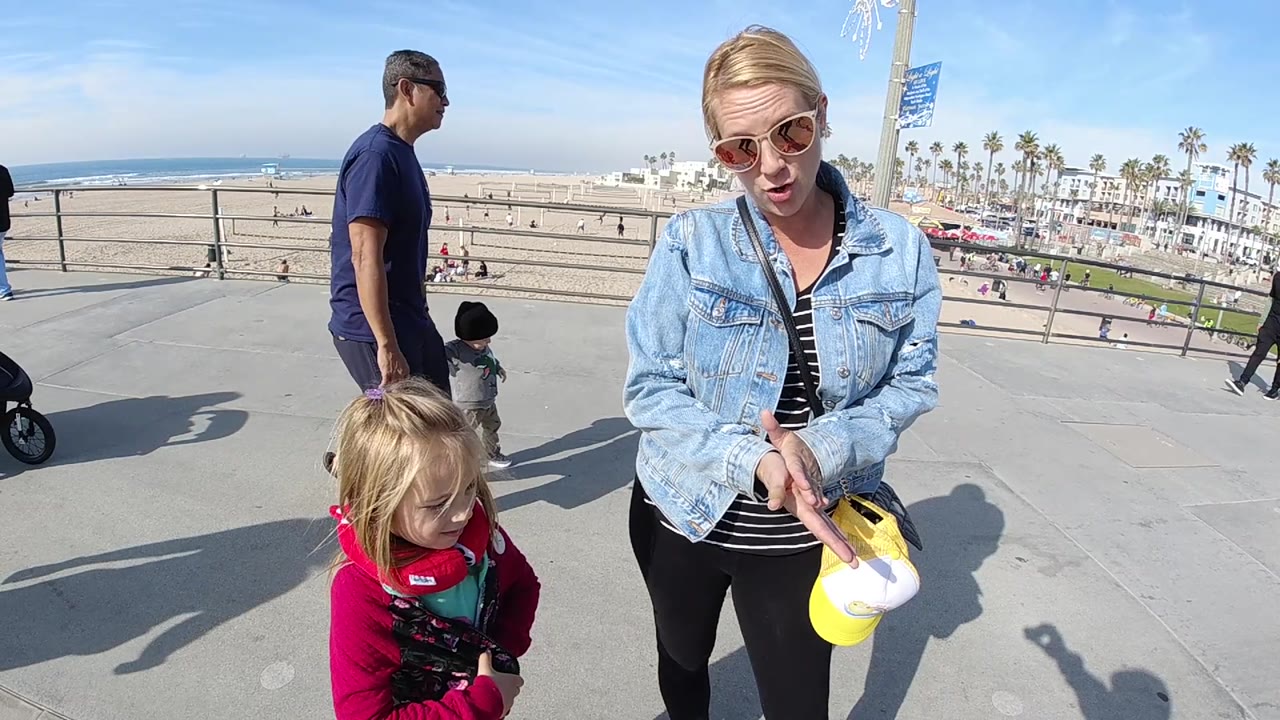 Little girl in red stands beside a woman on an elevated beach walkway.