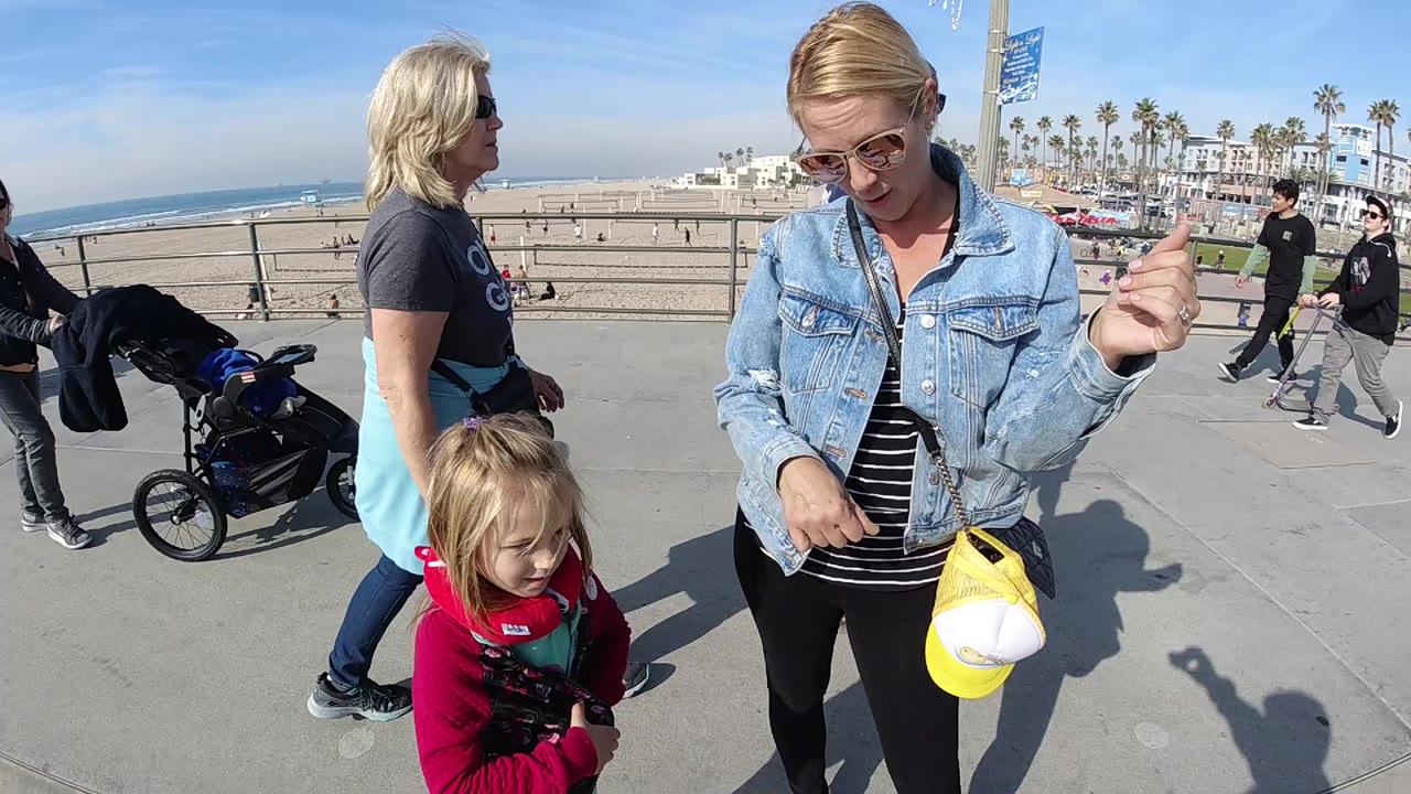 Woman looks downward while gesturing near a child on the beachfront path.