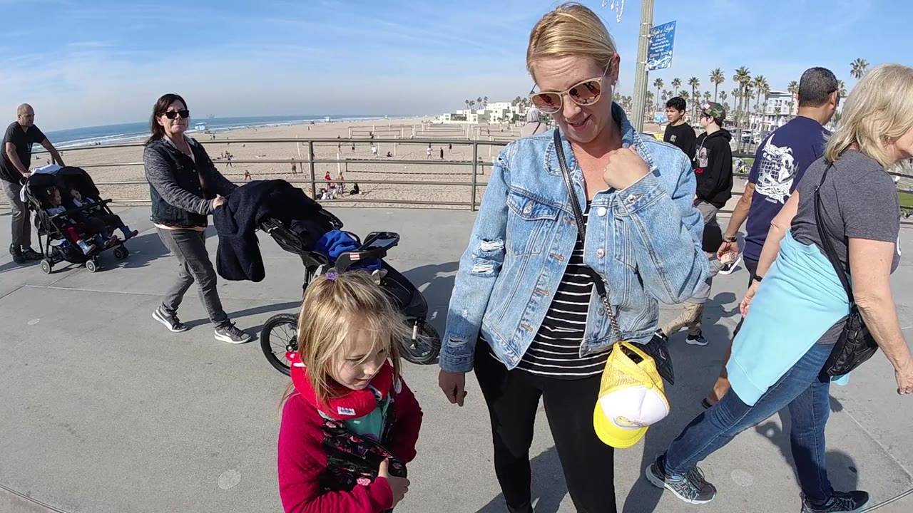 Family on promenade with beachgoers and strollers near the ocean.