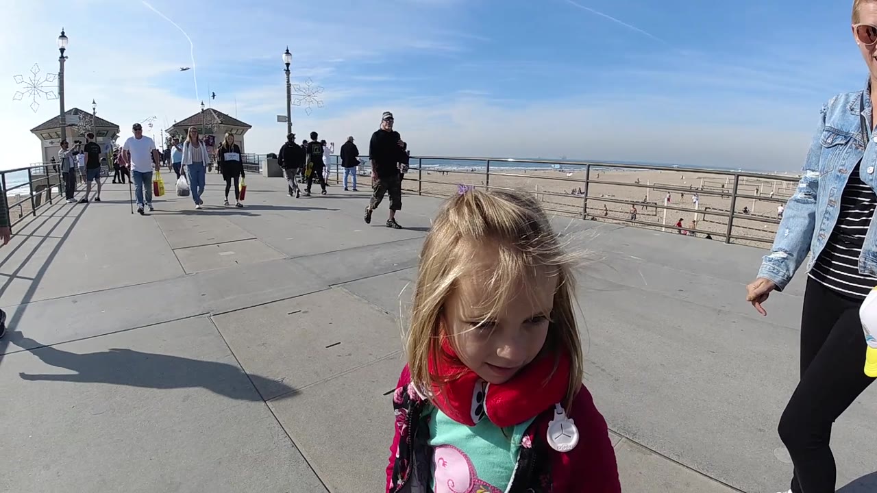 Young girl close to camera with pedestrians and pavilion structures along the beach walkway.