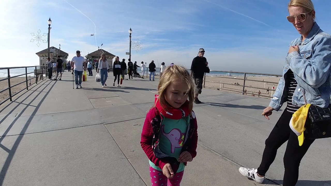 Girl looking downward while a woman walks beside her on a sunny pier.