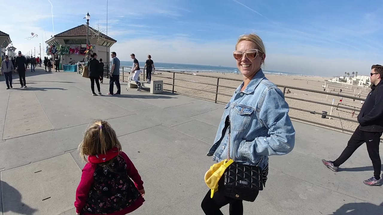 Smiling woman beside a child on a sunny pier walkway.