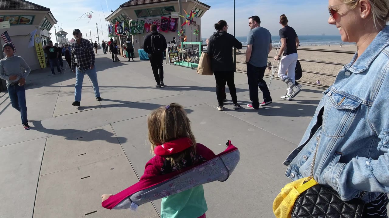 Child with a colorful item walks past a woman on a pier walkway.