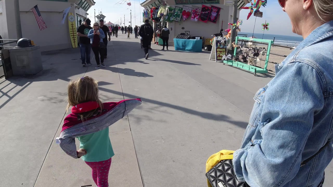 Child walking ahead with inflatable dolphin as woman is cropped at the side.