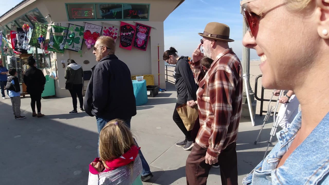 Man in hat and pedestrians passing a beachside vendor display.