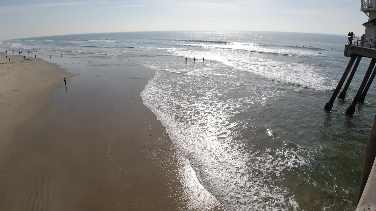 Sunlit waves spread across wet sand with beachgoers scattered near the waterline.