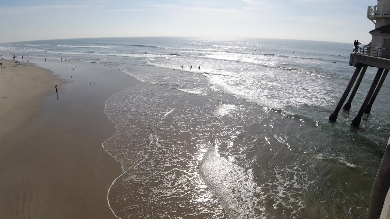 Foamy shoreline curves across wet sand with people far down the beach.