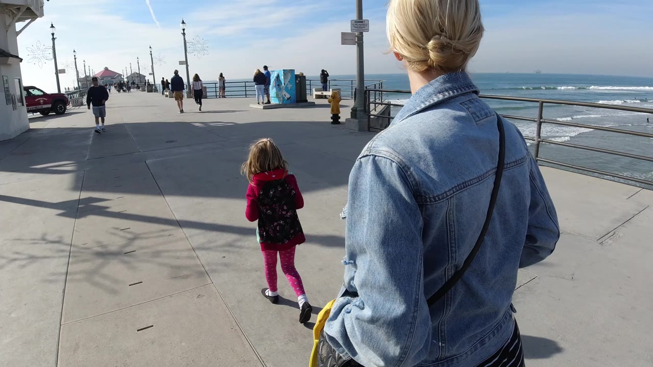 Child and woman continue along the pier beside the ocean.