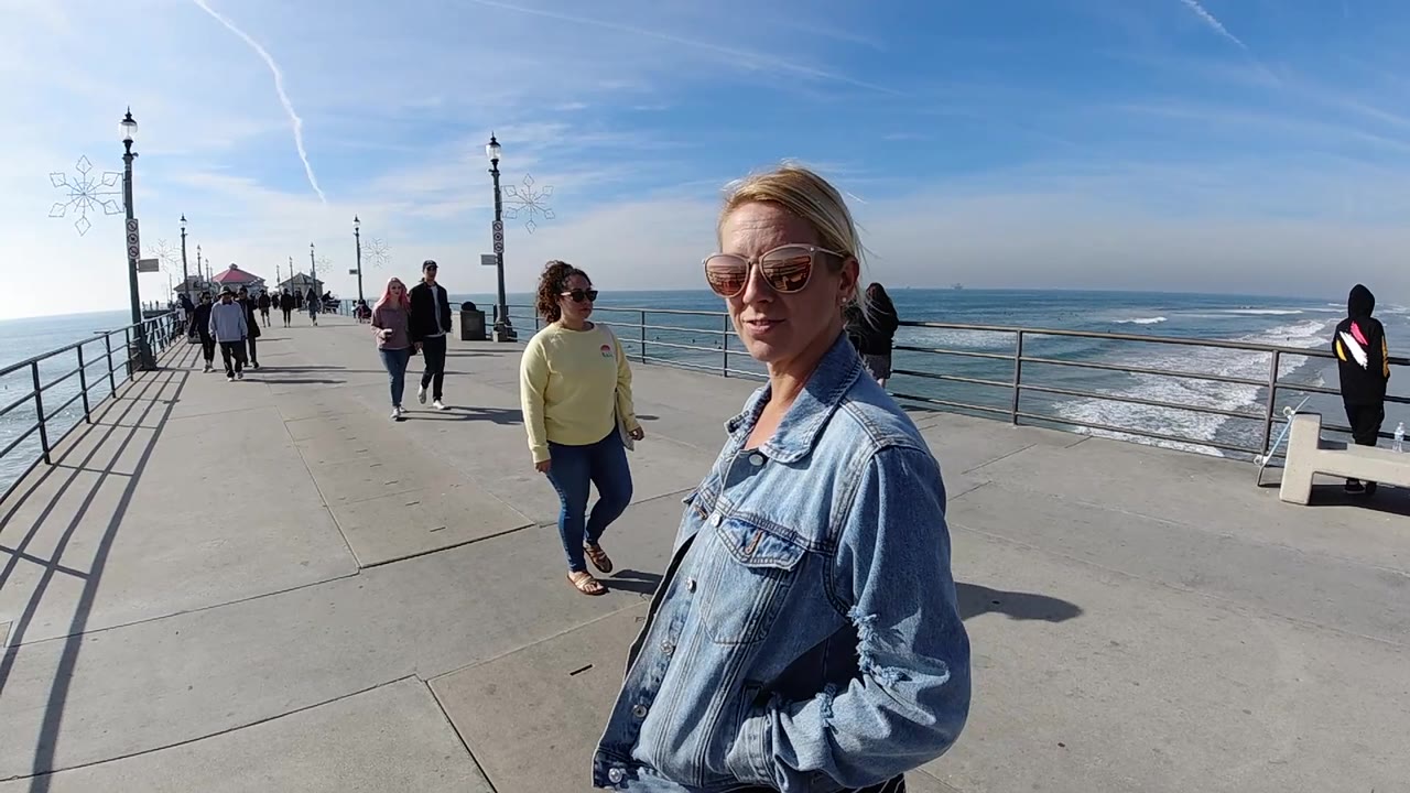 Close woman on pier with pedestrians and ocean railings behind her.