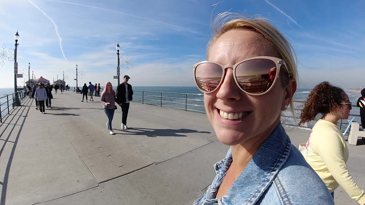 Smiling woman in sunglasses with pier walkers and surf behind