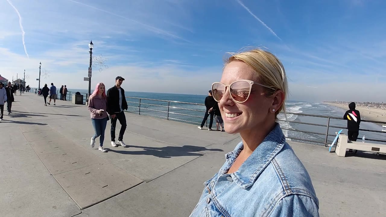 Side view of smiling woman on ocean walkway with people walking nearby.
