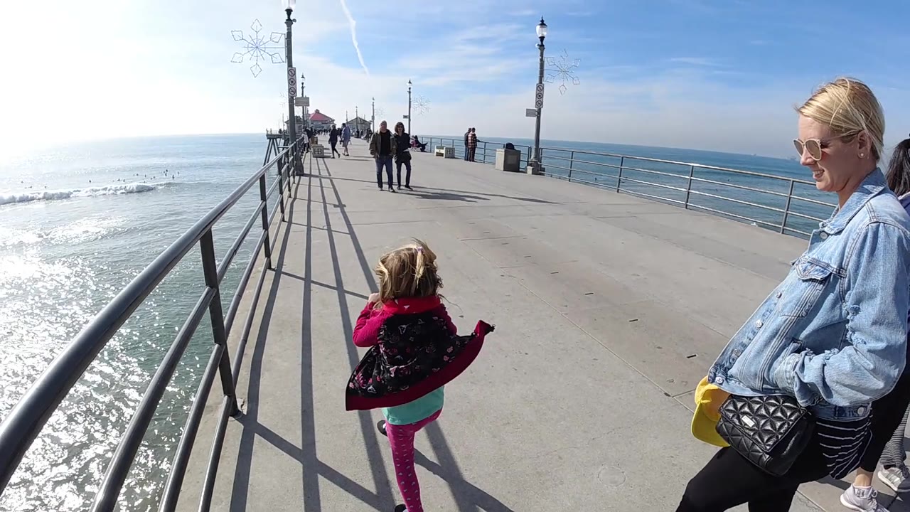 Girl turns near the railing while a woman stands on the pier in strong sunlight.