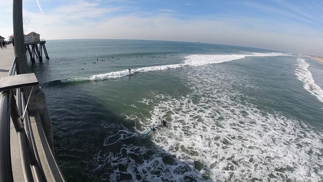 Breaking wave line beside a pier over green-blue water.