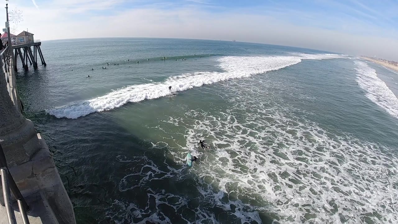 Pier-side ocean view with whitewater and people in the surf.