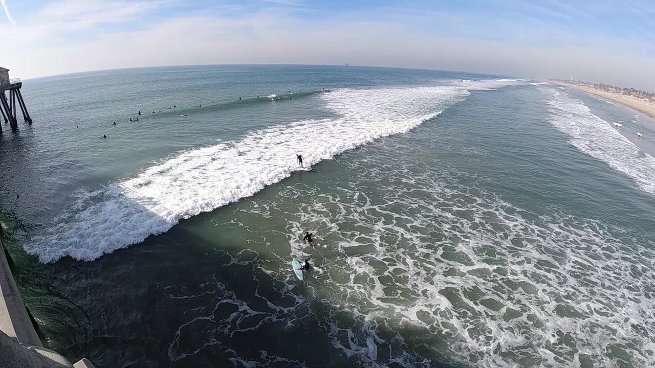 Foam patterns fill the lower Huntington Beach water while a clean wave band cuts across the middle distance and the beach remains visible beyond the open ocean.