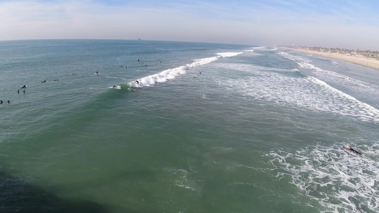 Surfer continues along the breaking wave while other surfers wait farther offshore.