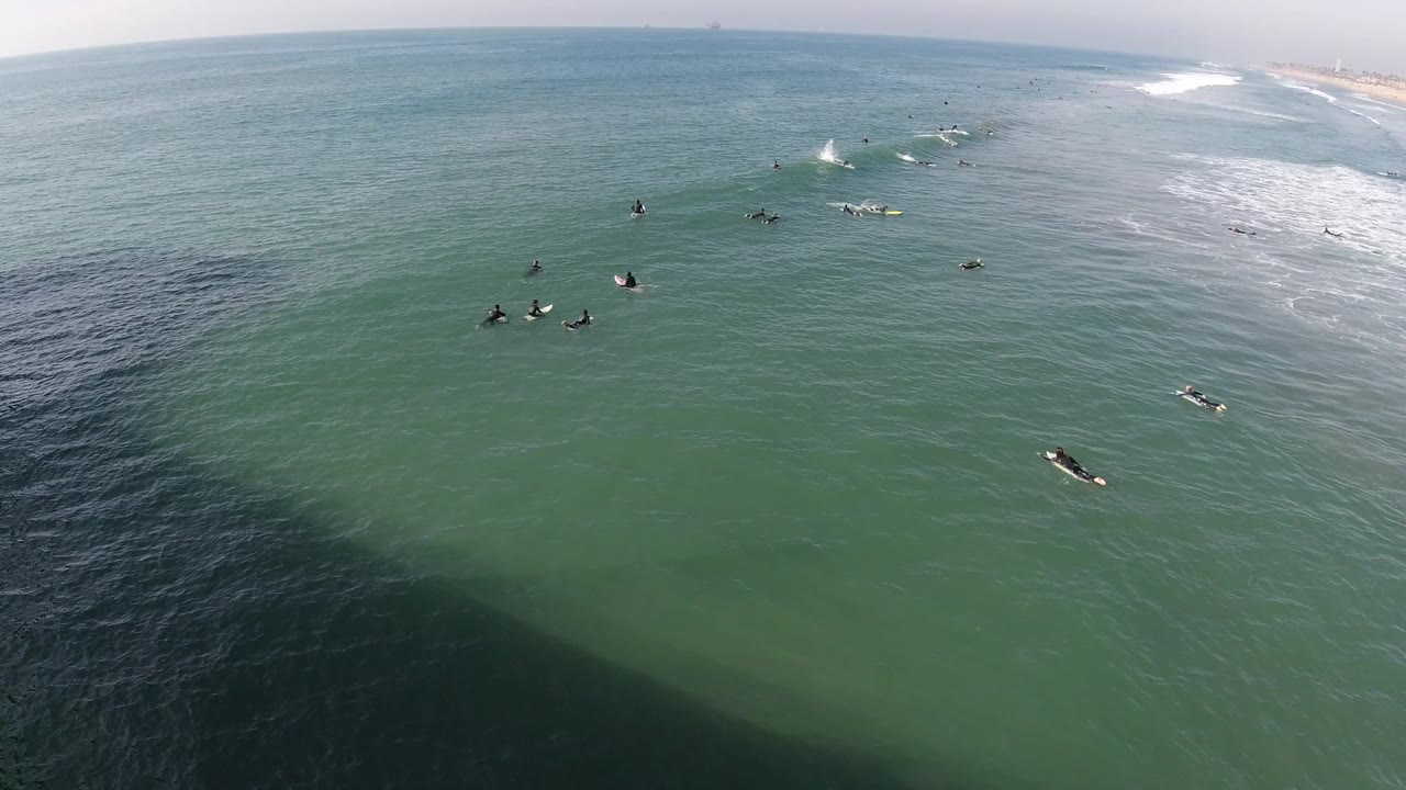 Surfers sit and paddle in open water as waves break near the beach.
