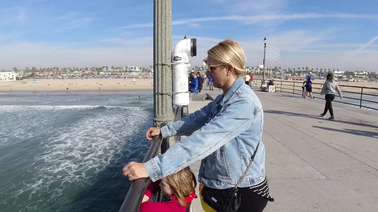Family at pier railing with surf below and pedestrians on walkway.
