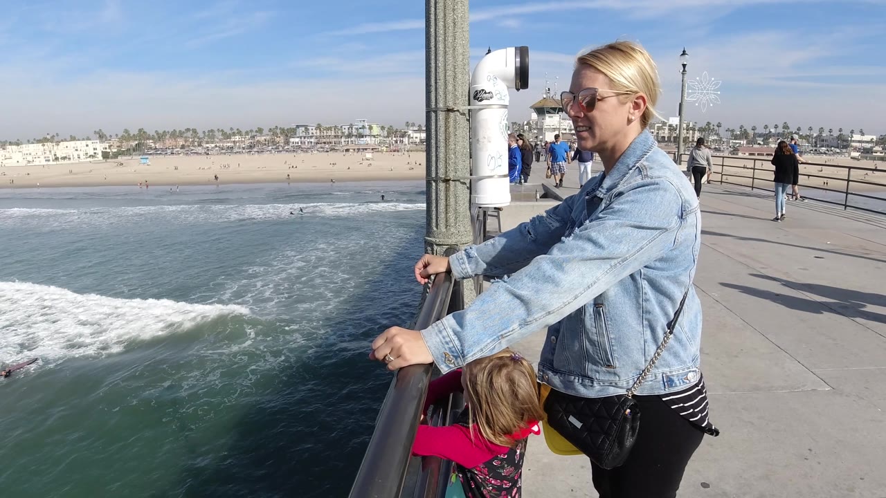 Woman and child leaning near pier rail above surf
