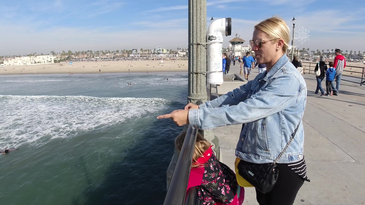 Woman pointing from pier railing toward surf below.