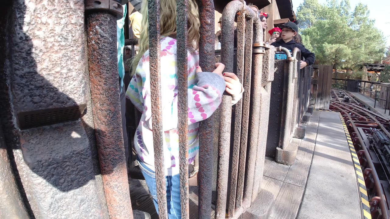 Ride queue railings with children waiting near coaster tracks