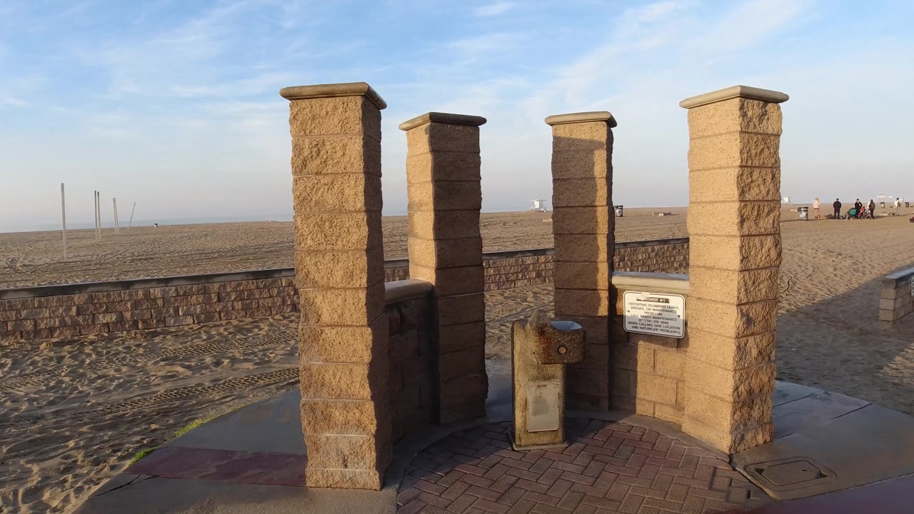 Close view of tall stone pillars, beach sand, and low wall.