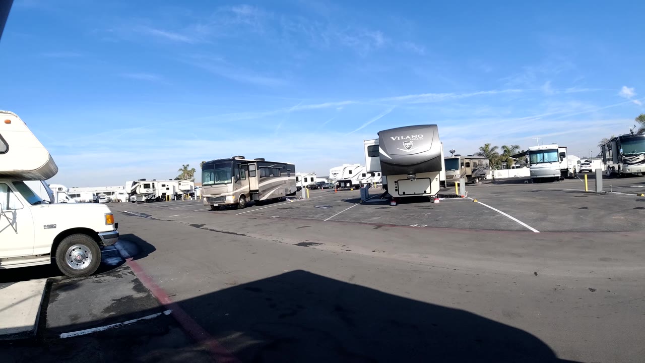 A large RV faces the camera in a Huntington Beach parking lot while other motor homes sit across the background, with no visible people.