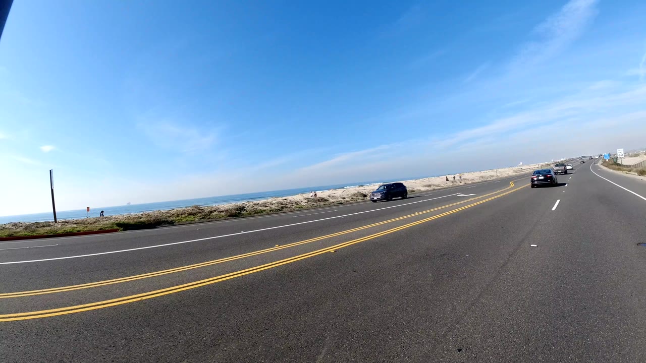 Coastal roadway with sandy shoulder and cars ahead