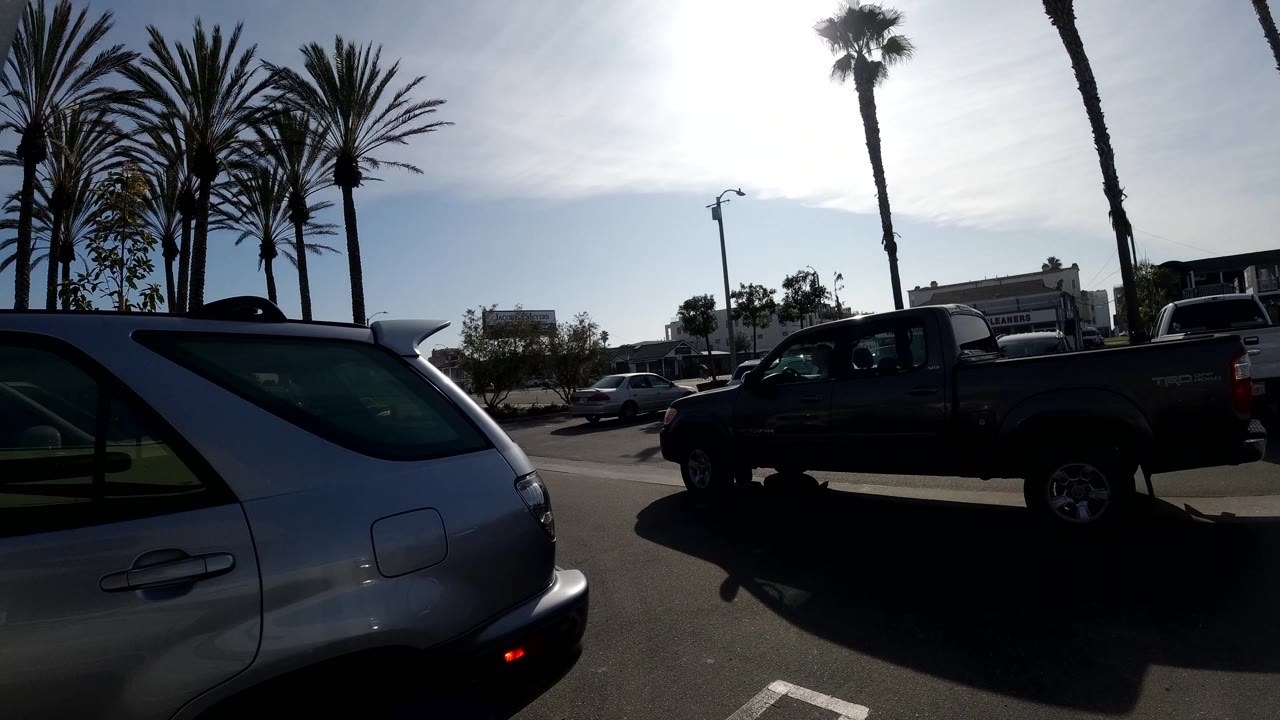 A dark pickup truck moves across the Huntington Beach street scene, partly silhouetted against the bright sky, with the silver SUV still cropped at the lower left.