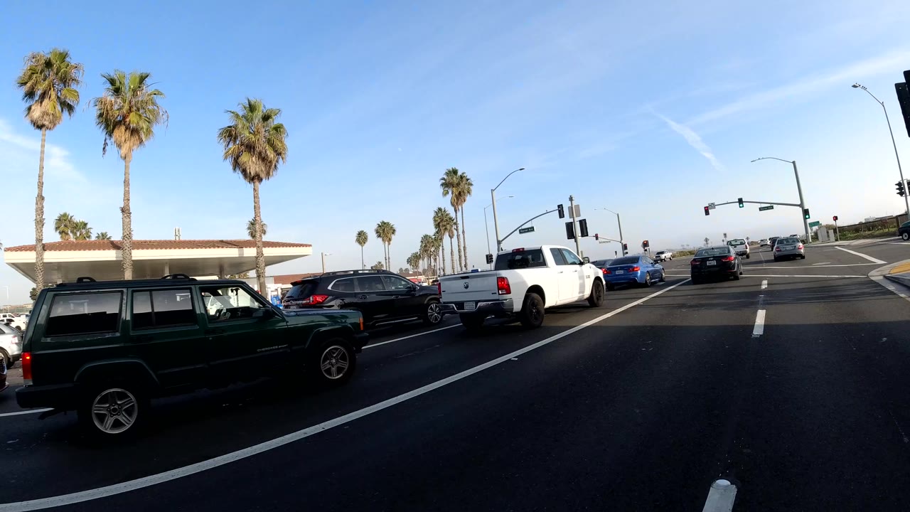 Bolsa Chica, California traffic scene with cars, pickup trucks, palm trees, signal lights, lane markings, and no clearly visible faces.