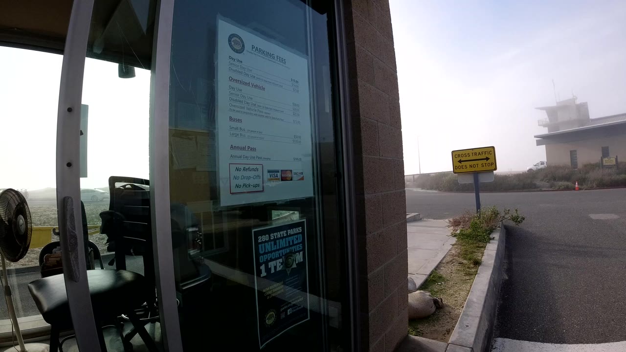 A glass door with parking fee notices and reflections stands beside a bright hazy road in Bolsa Chica, California, with no visible people.
