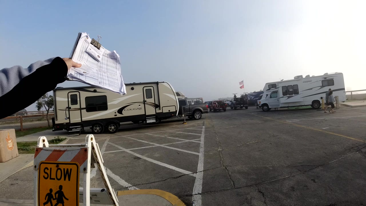 Hand holding papers above an RV lot with trailers and vehicles.