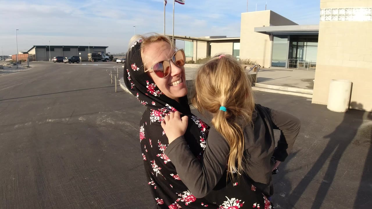 Woman smiles while carrying a young girl near a building entrance.