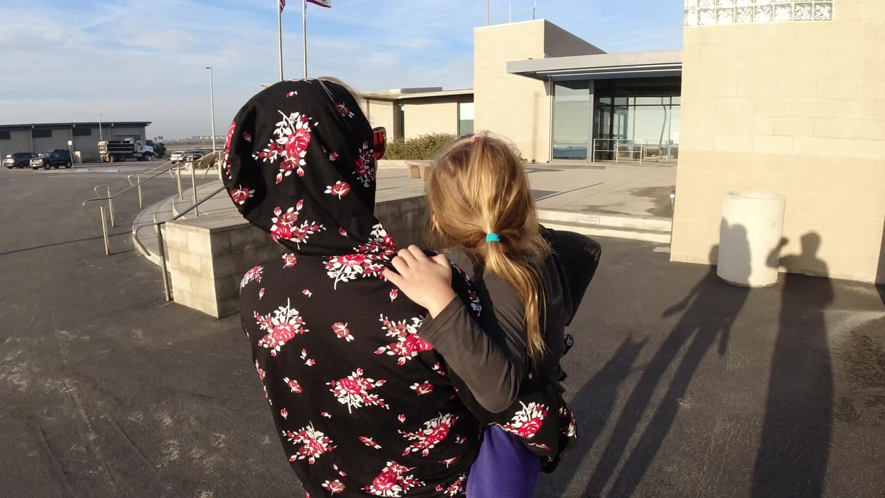 Rear view of woman carrying child beside a low wall.