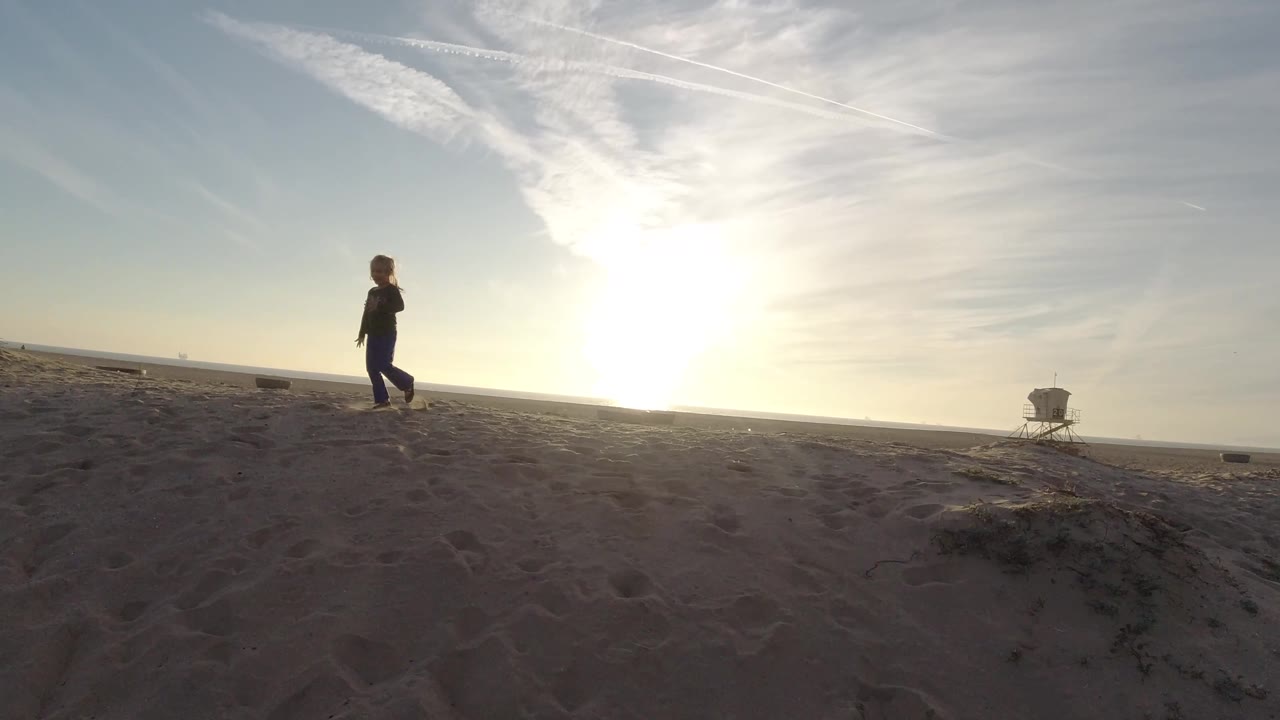 Young girl walking across beach in front of bright horizon.