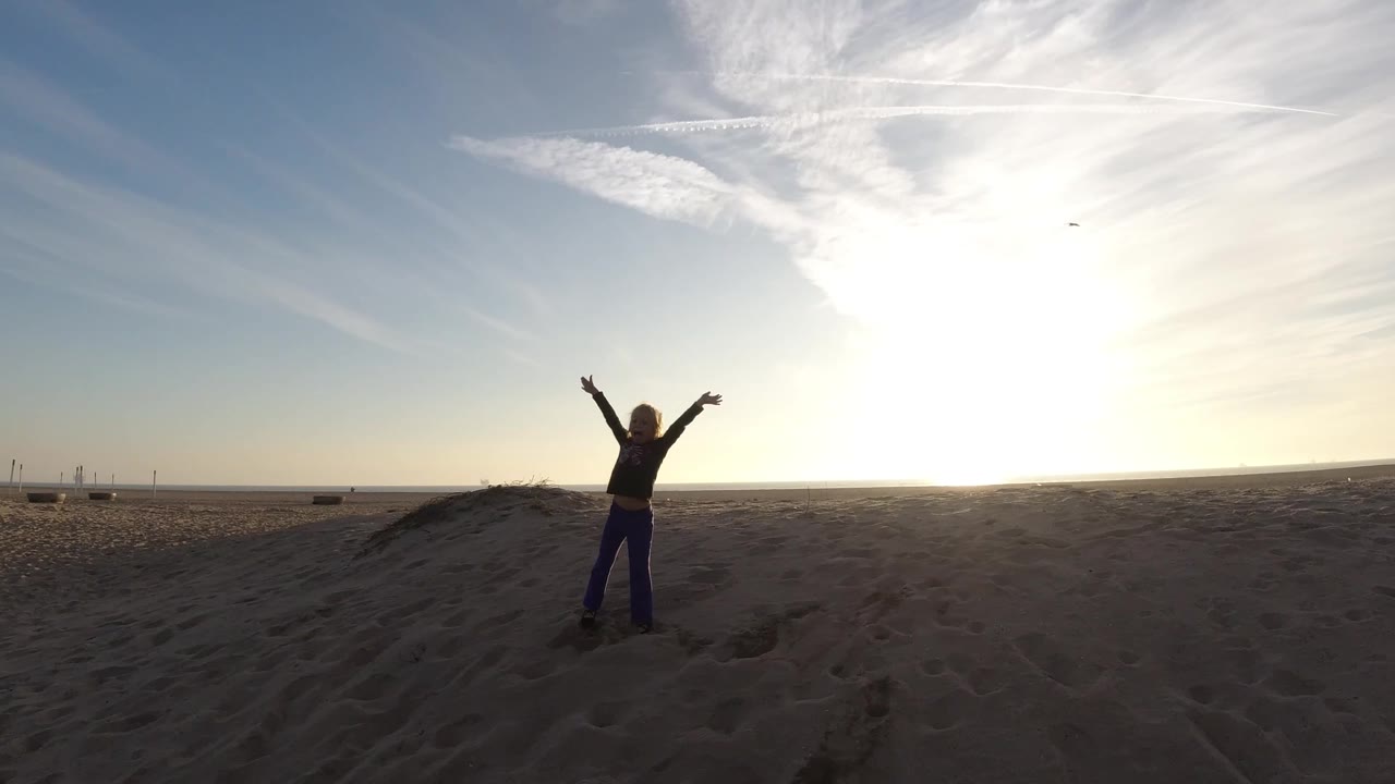 Backlit person with raised arms on a sandy beach.