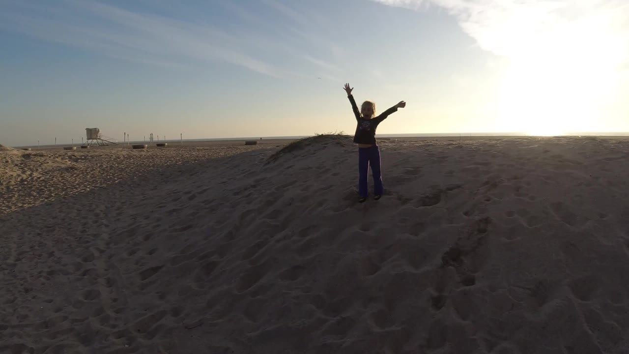 At Bolsa Chica, California, the person remains centered on the dune, with dark foreground sand texture and a bright sunlit horizon behind them.