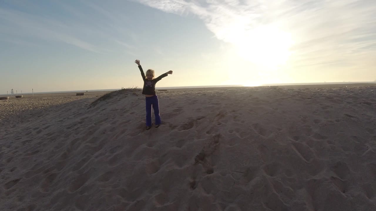 Person silhouetted on dunes with sunrise glare over the beach.