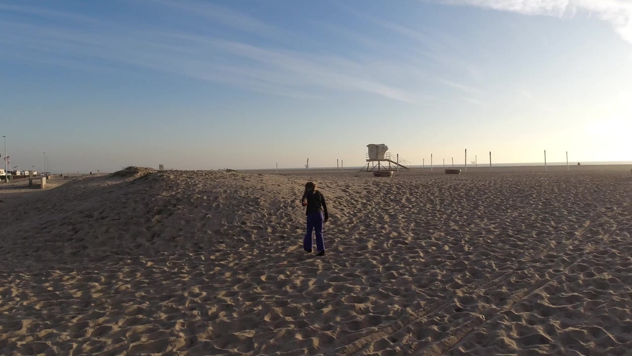 Girl on open sand with lifeguard tower and pale sky behind her.