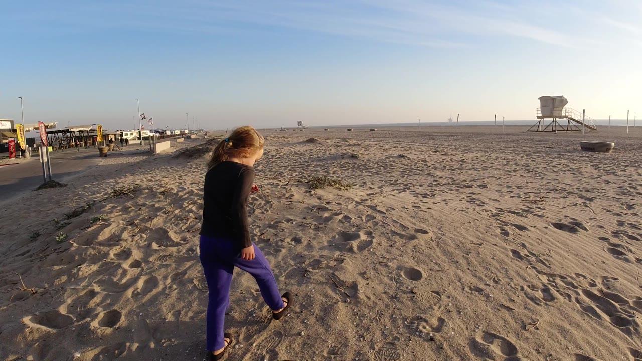 Girl steps across sand with beach access area and lifeguard tower behind.